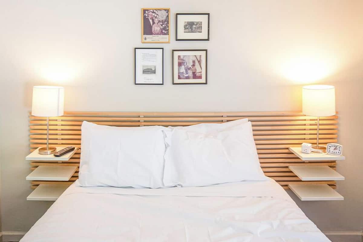 A neatly made bed with white linens, two bedside tables with lamps, and framed pictures on the wall.