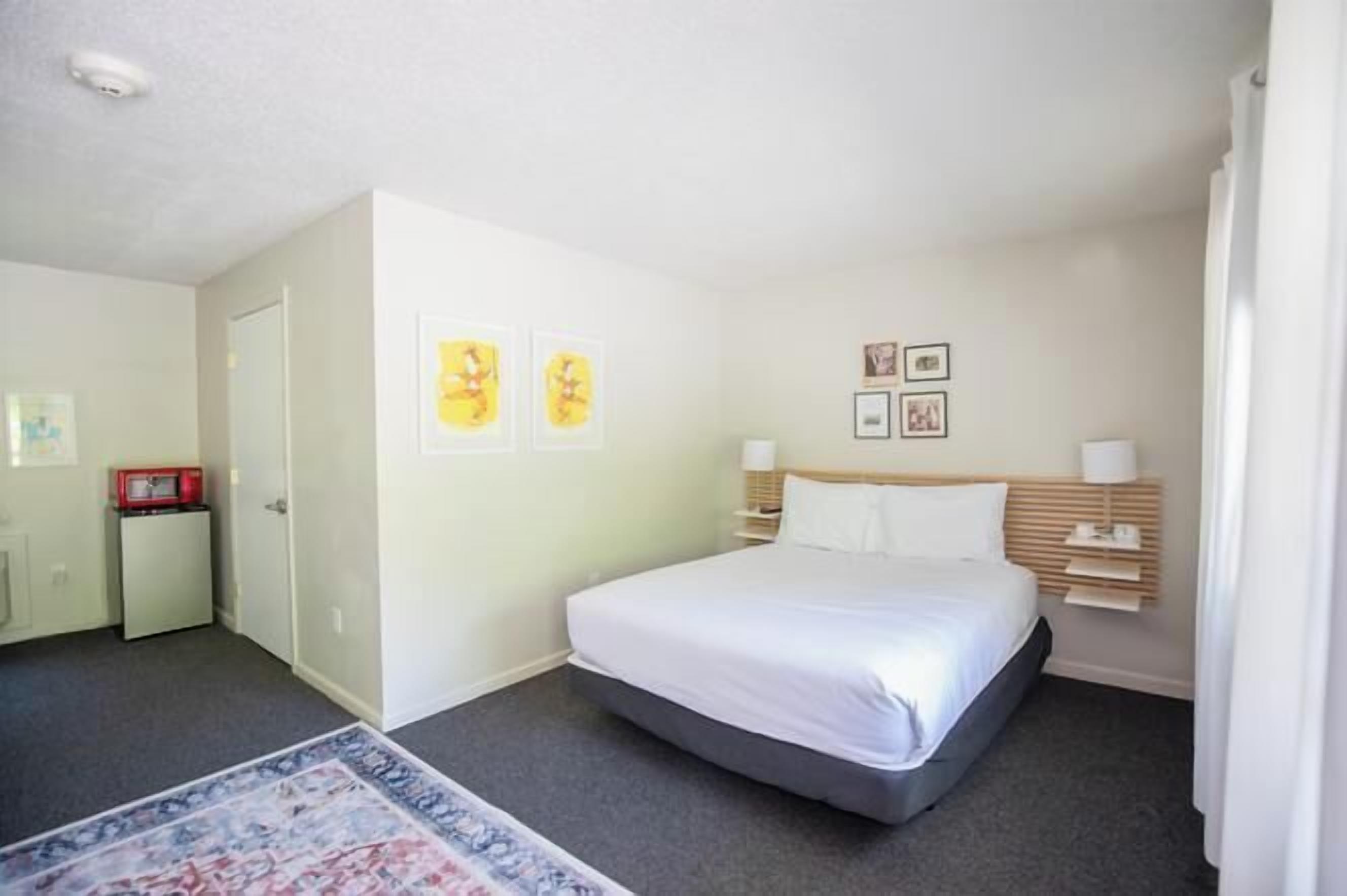 A hotel room with a bed, bedside tables, a nightstand, a small desk, and a chair.