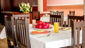Una mesa de comedor con platos de comida, un tazón de manzanas y un vaso de jugo de naranja.
