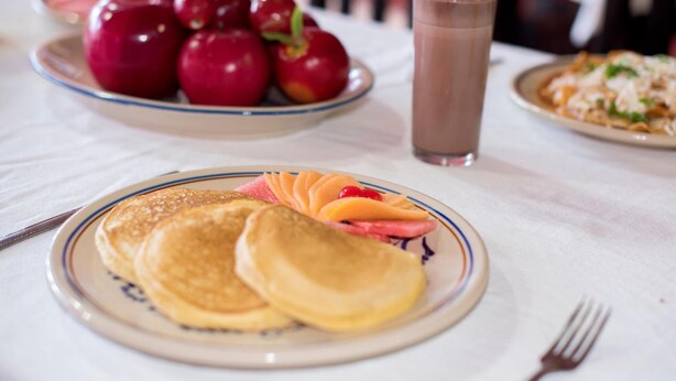 Desayuno con tortitas, manzanas y una bebida de chocolate sobre una mesa.