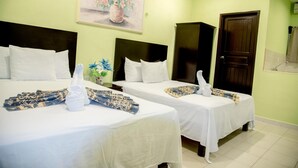 Habitación de hotel con dos camas, cada una con ropa de cama blanca y toallas decorativas. Encima de las camas hay un cuadro en la pared, y se ve un armario de madera en la esquina.