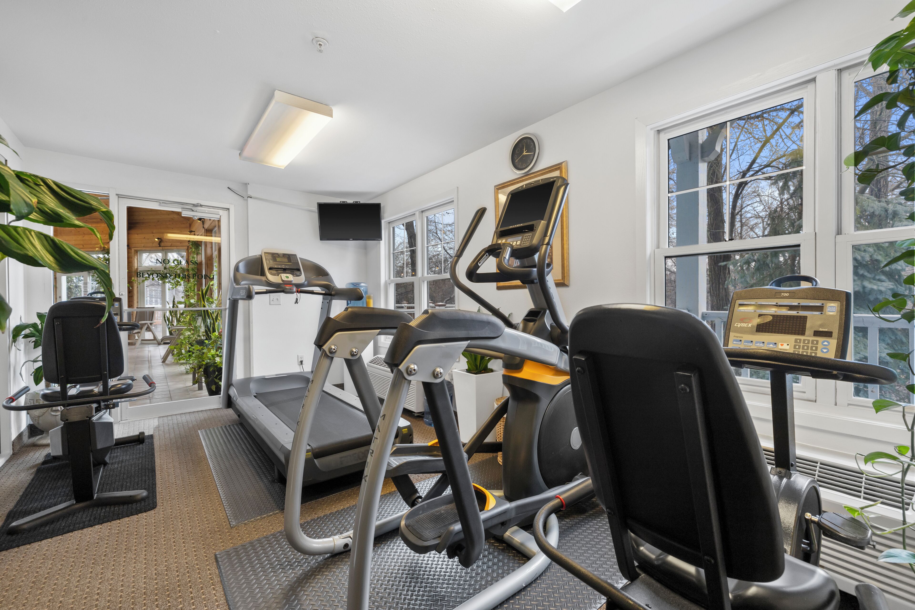 A gym with exercise equipment, large windows, and a clock on the wall.
