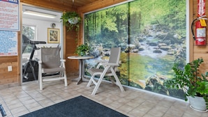 A room with a large window overlooking a forested area, a small table with chairs, a fire extinguisher on the wall, and a sign with pool rules.