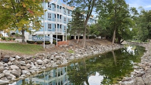 A hotel with a reflection in a pond, surrounded by trees and a stone wall.