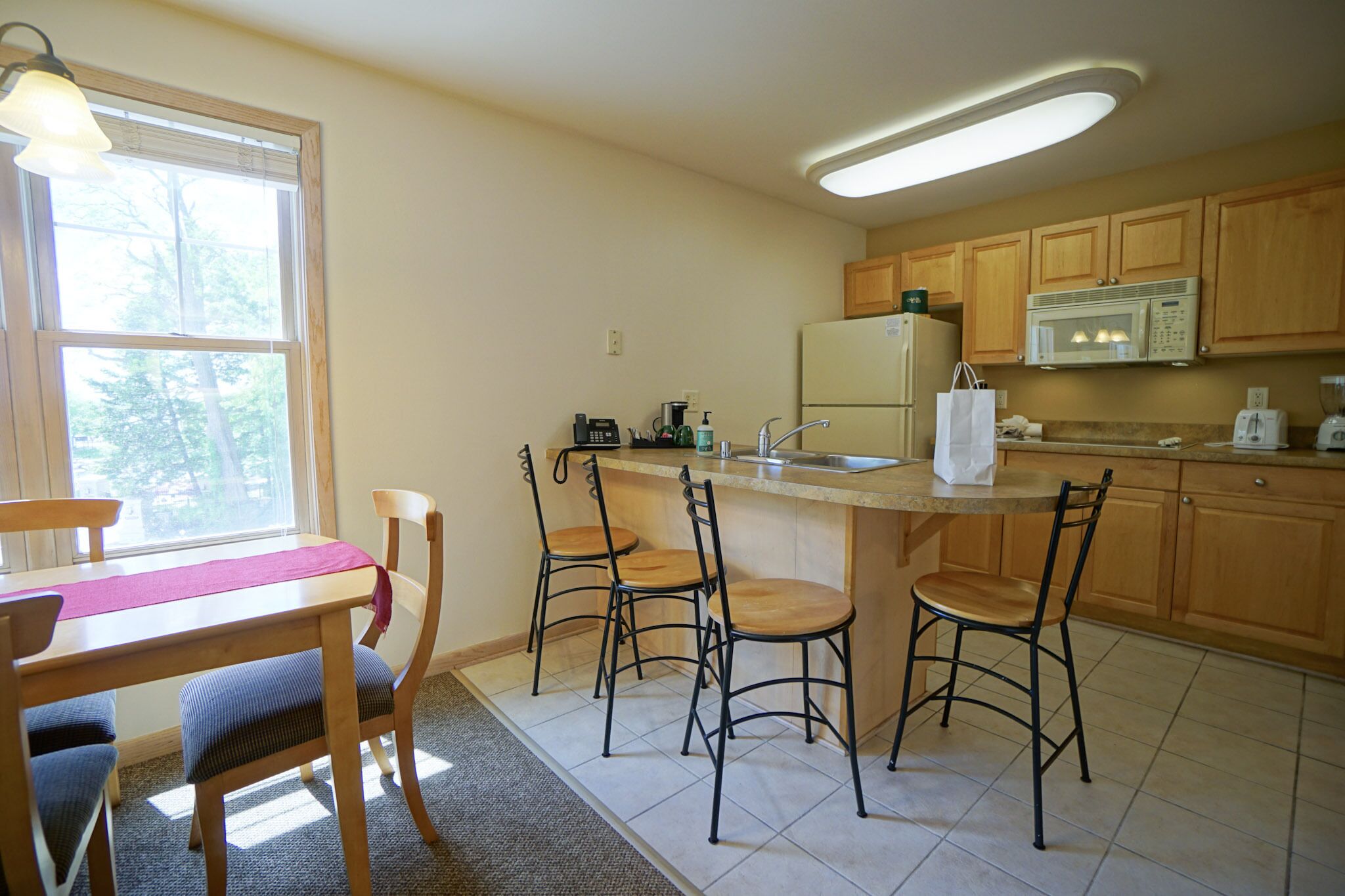 A kitchen with wooden cabinets, a refrigerator, a microwave, a sink, and a dining area with a table and chairs.