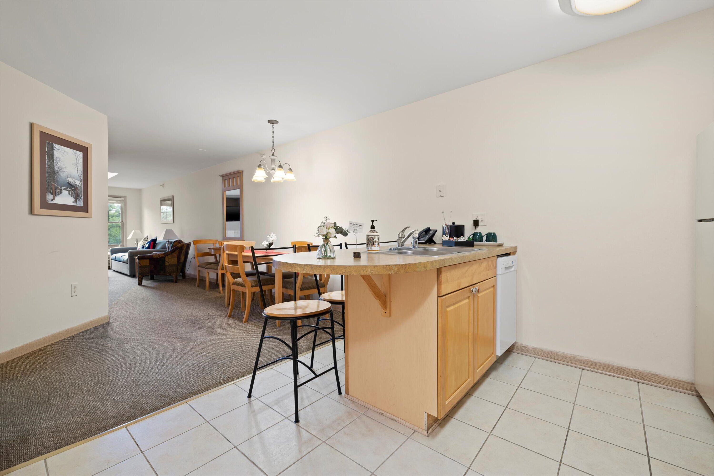 A modern kitchen with a central island, wooden cabinets, and a dining area with chairs.
