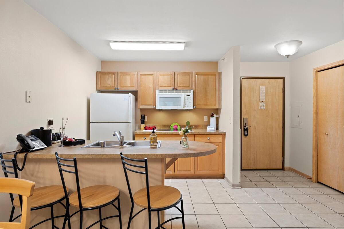 A compact kitchen with a central island, wooden cabinets, a microwave, and a refrigerator.