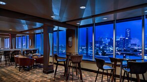 A modern bar area with a geometric patterned floor, large windows offering a city view, and contemporary furniture. - Ambassador Hotel Oklahoma City, Autograph Collection (Oklahoma City)