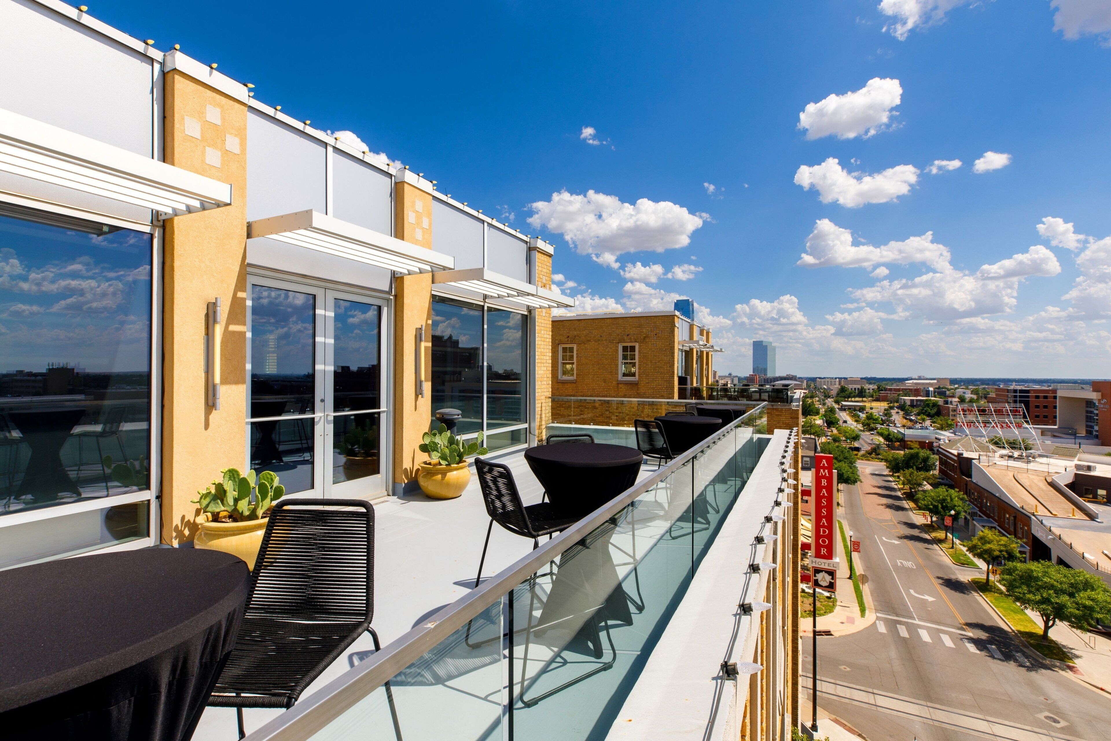 Una terraza en la azotea con mobiliario exterior, barandillas de cristal y vistas a la ciudad.