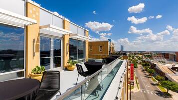 Una terraza en la azotea con mobiliario exterior, barandillas de cristal y vistas a la ciudad.