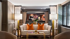 A modern living room with a sofa, two armchairs, a coffee table, and a dining table. There are lamps, a vase with flowers, and a painting on the wall. - Ambassador Hotel Oklahoma City, Autograph Collection (Oklahoma City)