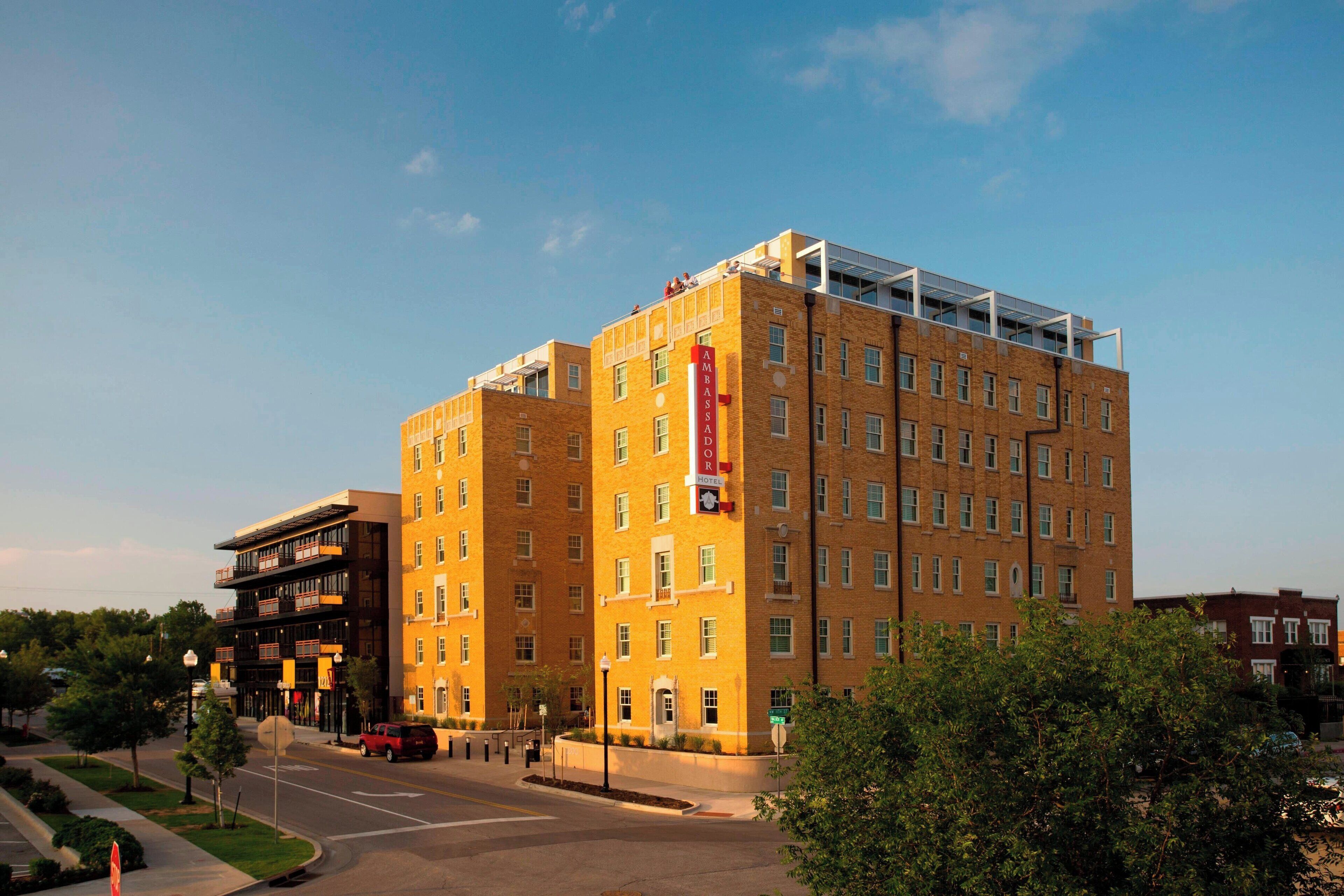 Un hôtel à plusieurs étages, reconnaissable à son grand panneau « Ambassador », qui présente une architecture moderne avec une combinaison de façades en brique et en verre.