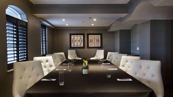 A conference room with a long table, white upholstered chairs, and two framed artworks on the wall.