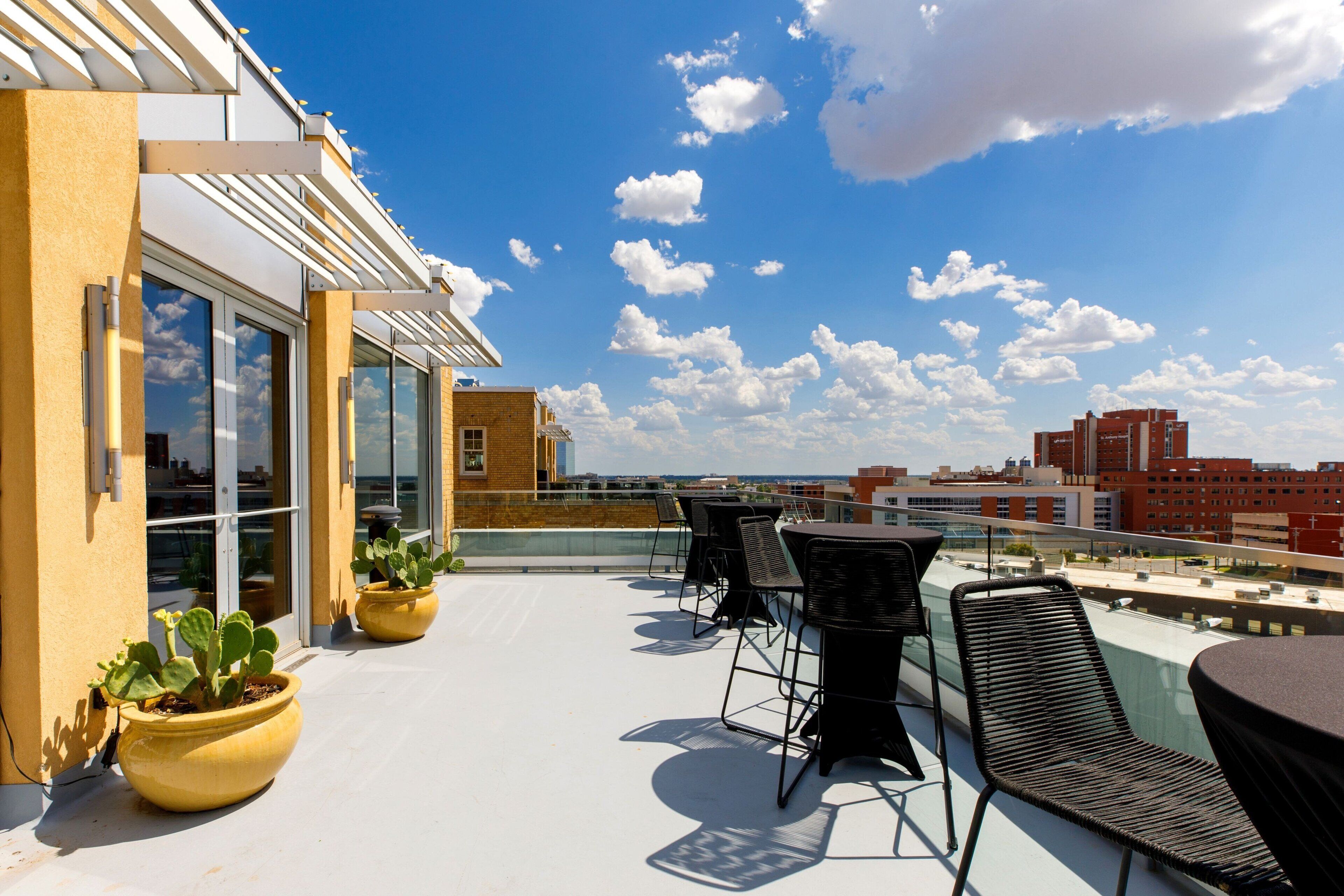 A rooftop terrace with outdoor seating, potted plants, and a view of the city skyline.