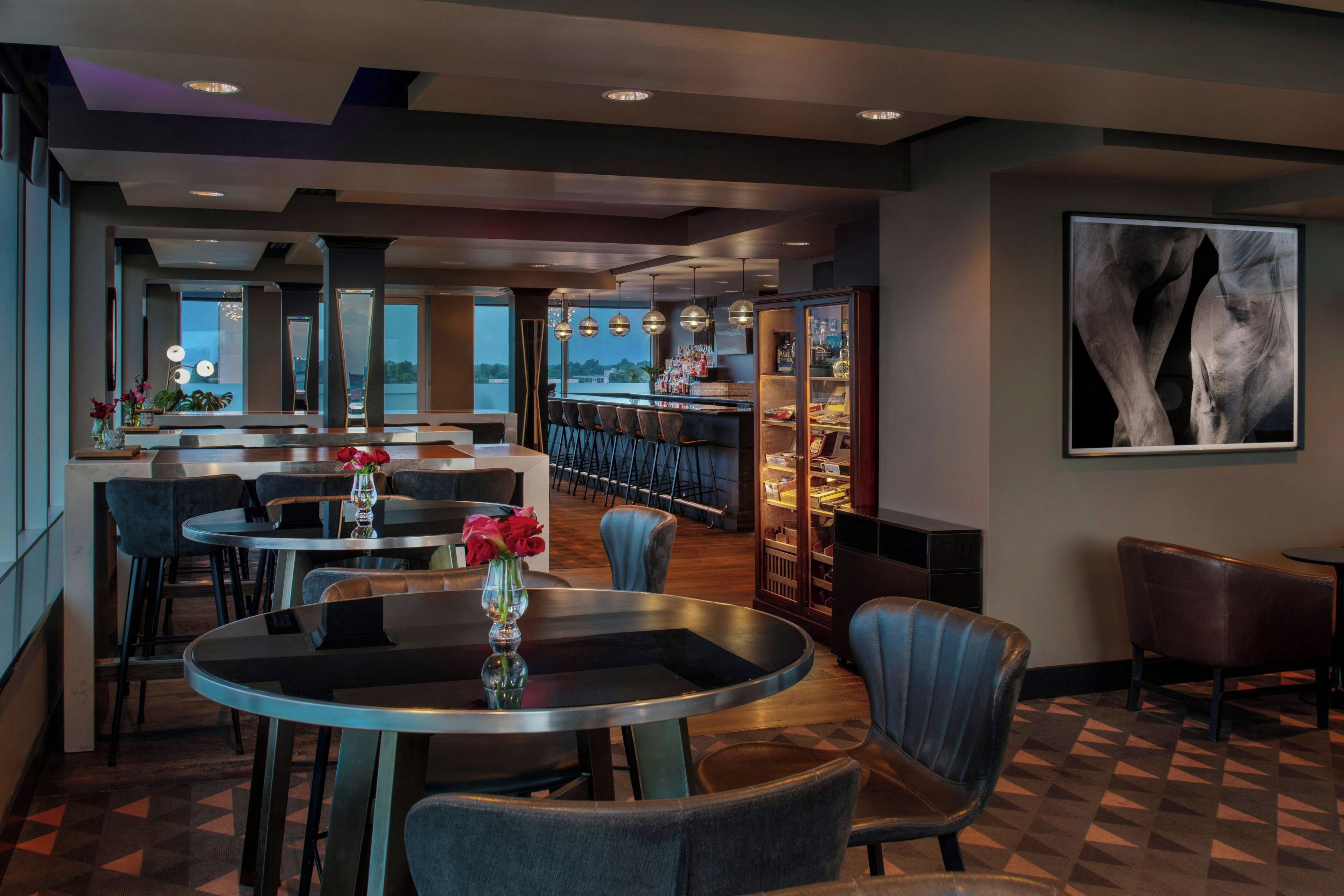 A modern restaurant with round tables, bar seating, and a view of the cityscape.