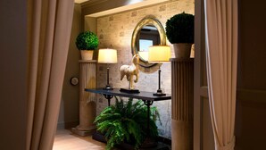 A hallway with a mirror, two lamps, a potted plant, and a statue.
