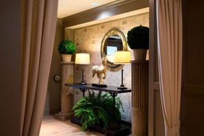 A hallway with a mirror, two lamps, a potted plant, and a statue.