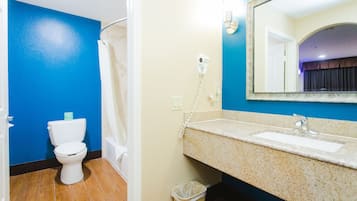 A bathroom with a blue wall, a white toilet, a shower curtain, a sink with a mirror, and a hairdryer on the wall.