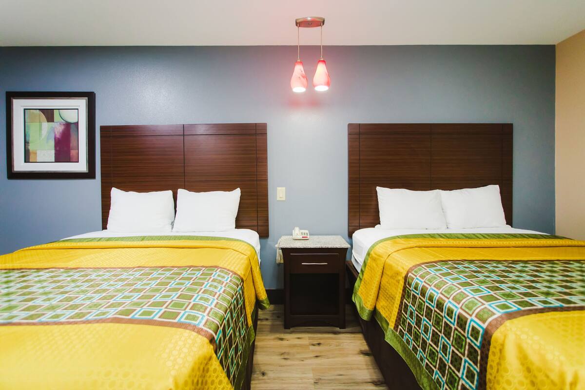A hotel room with two beds, a nightstand, and a wall-mounted light fixture.