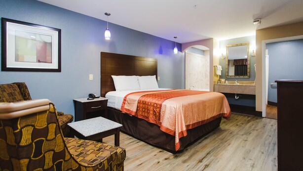 A hotel room with a bed, a chair, a nightstand, a mirror, and a framed picture on the wall. - Home Place Inn (Houston)
