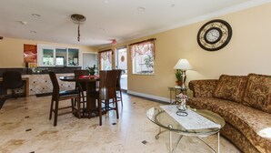 A dining area with a table and chairs, a sofa, a clock, and a window with curtains. - Home Place Inn (Houston)