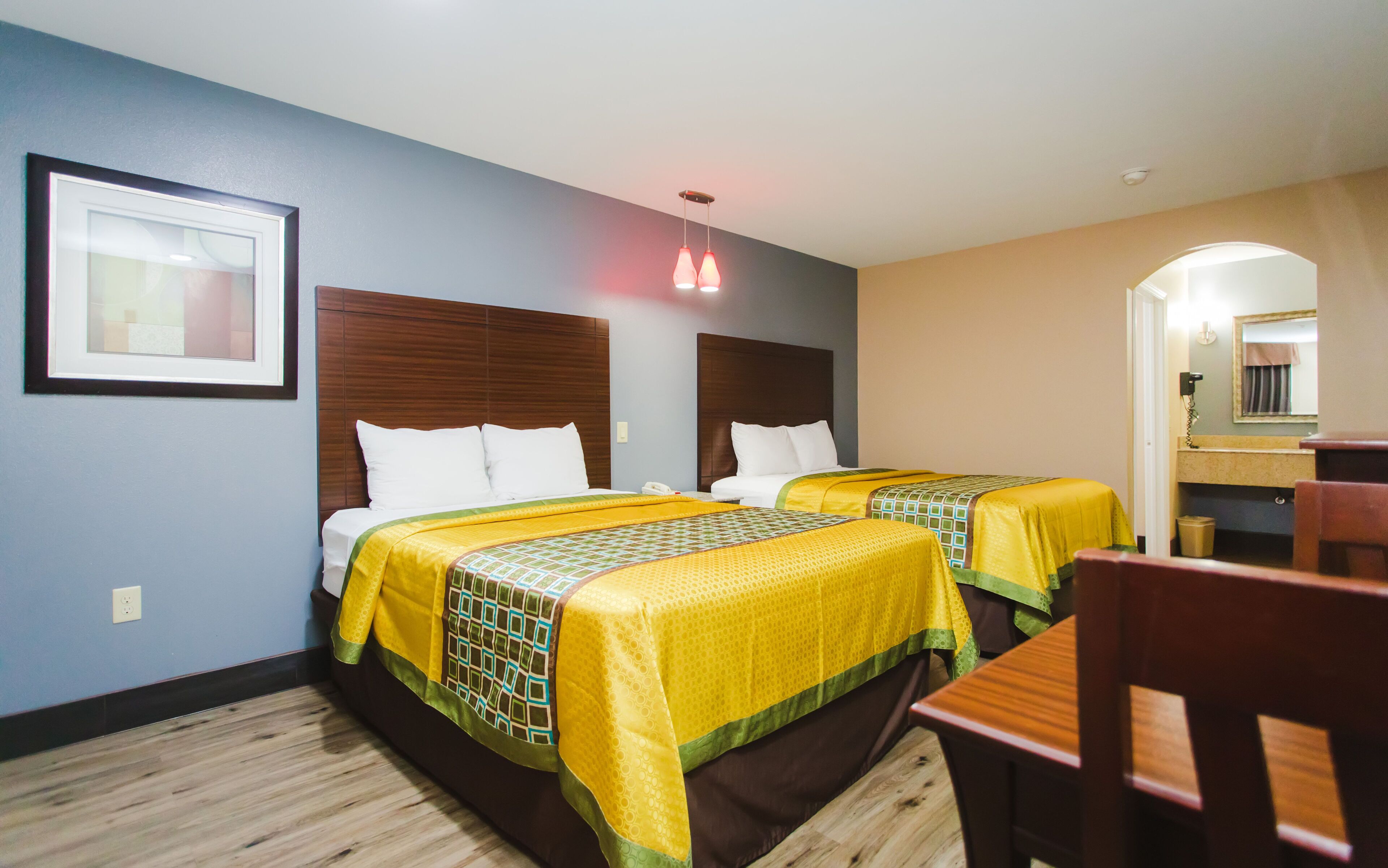 Habitación de hotel con dos camas, cabecera de madera, un cuadro enmarcado en la pared, un escritorio y un espejo.