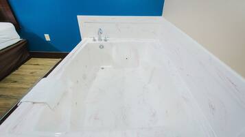 A large, empty bathtub in a room with blue walls and a wooden floor.