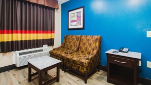 A room with a patterned sofa, a small table, a bedside table with a phone, and a wall-mounted air conditioner. - Home Place Inn (Houston)
