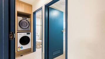 Ein kleiner Waschraum mit Waschmaschine und Trockner, einer Toilette und einer blauen Tür.