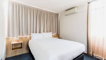 Ein Hotelzimmer mit einem großen Bett, einem Nachttisch, einer Klimaanlage und einem Fenster mit Vorhängen.