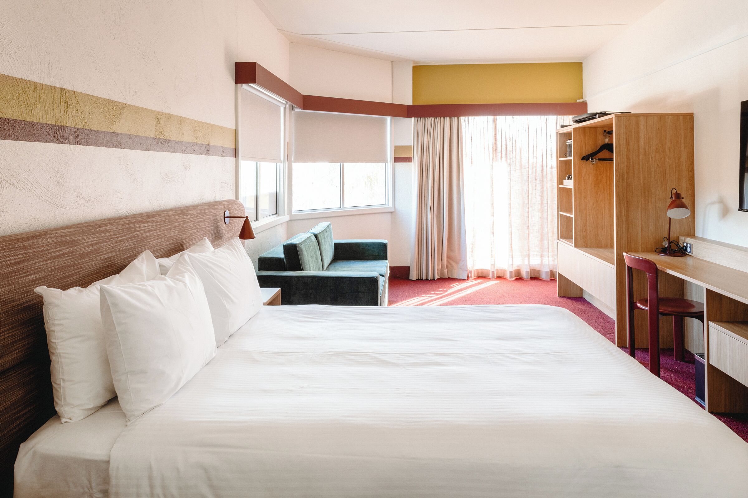 A hotel room with a large bed, a desk, a chair, a wardrobe, and a window with curtains.
