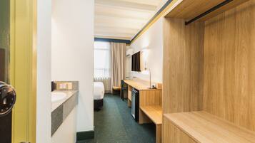 A hotel room with a bed, a desk, a sink, and a mirror.