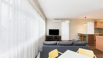 Una sala de estar moderna con un sofá gris, un televisor de pantalla plana y un comedor con una mesa blanca y sillas amarillas.
