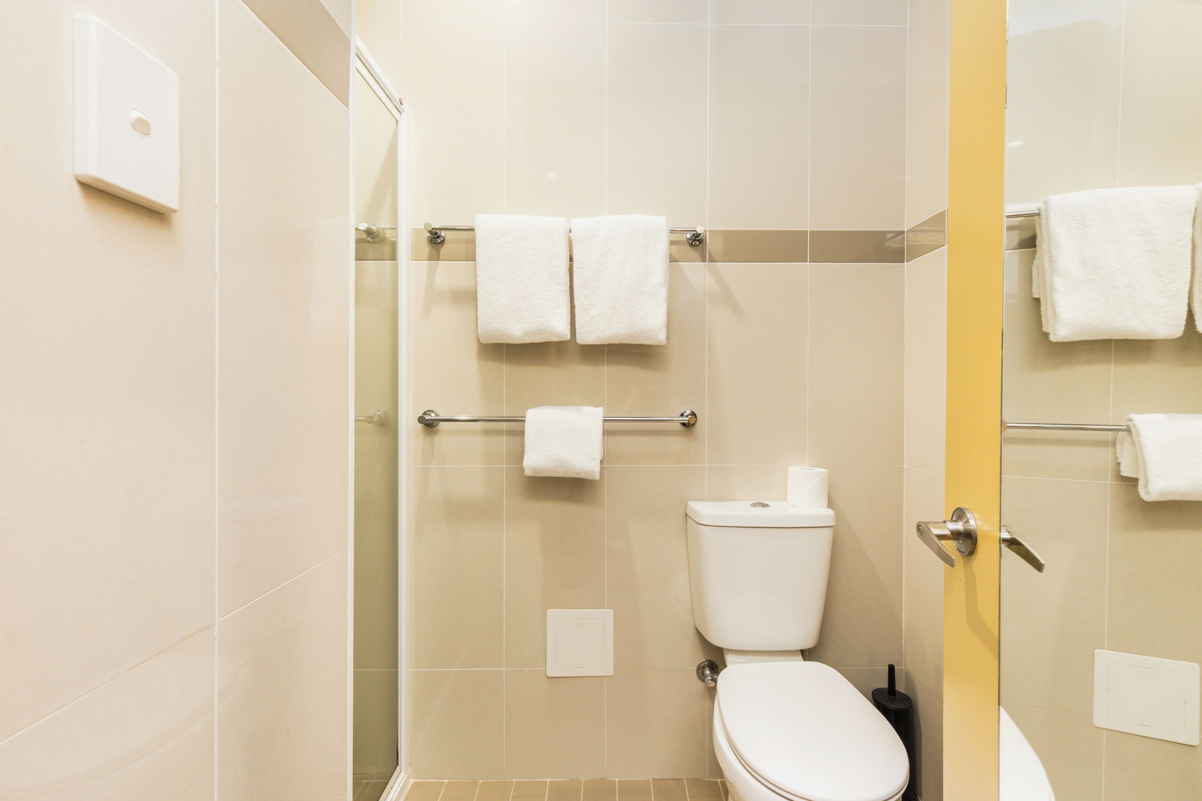 A bathroom with a toilet, a shower, and a towel rack with two towels.