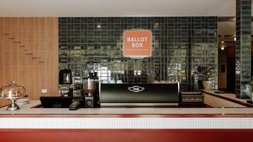 A coffee shop counter with a ballot box sign, a coffee machine, and a WeGA logo.