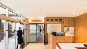 A reception area with a wooden reception desk, a fire indicator panel, and a map on the wall. - Statesman Hotel (Curtin)