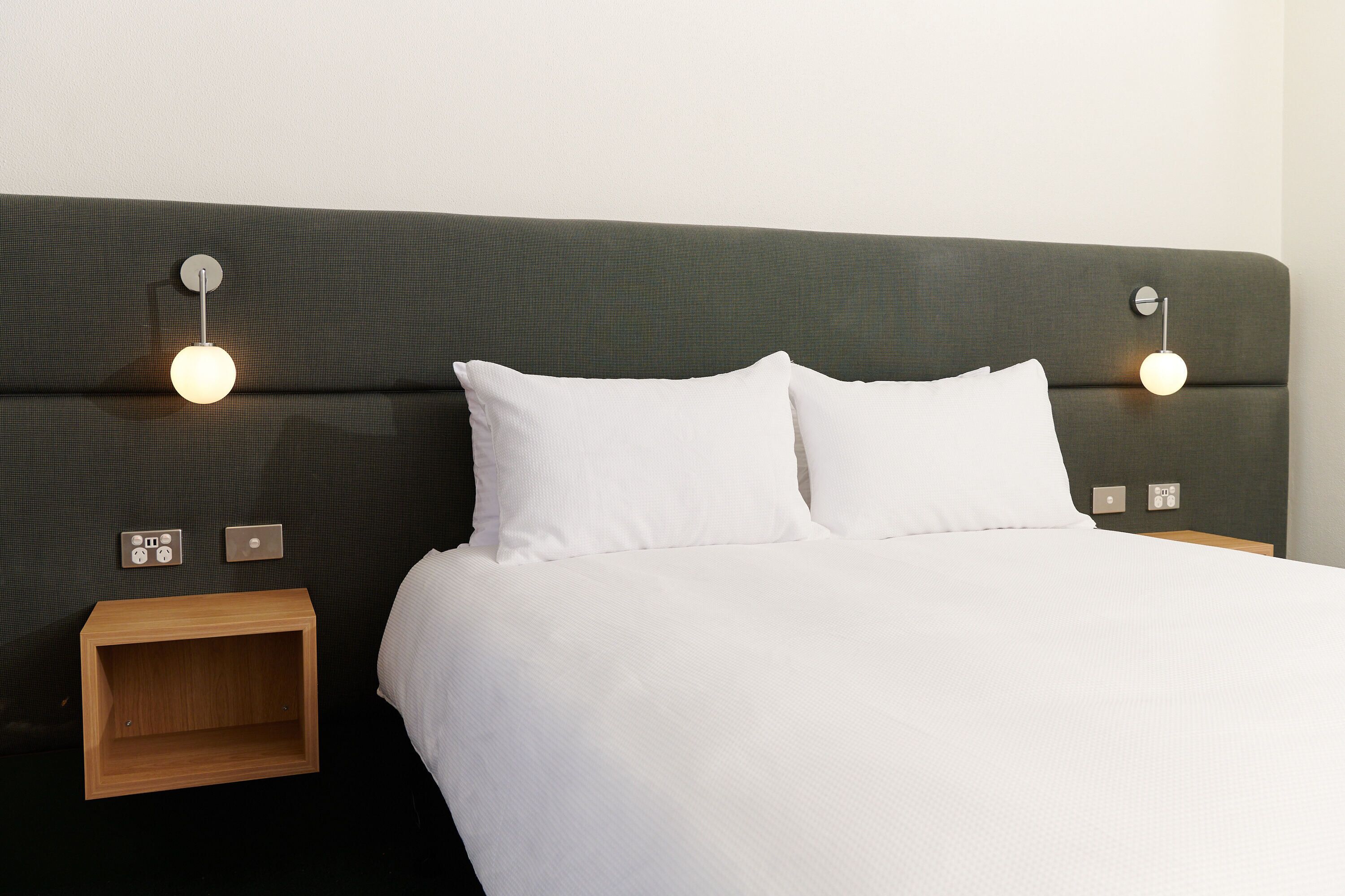 A neatly made bed with white linens, two bedside tables with lamps, and a dark green headboard.