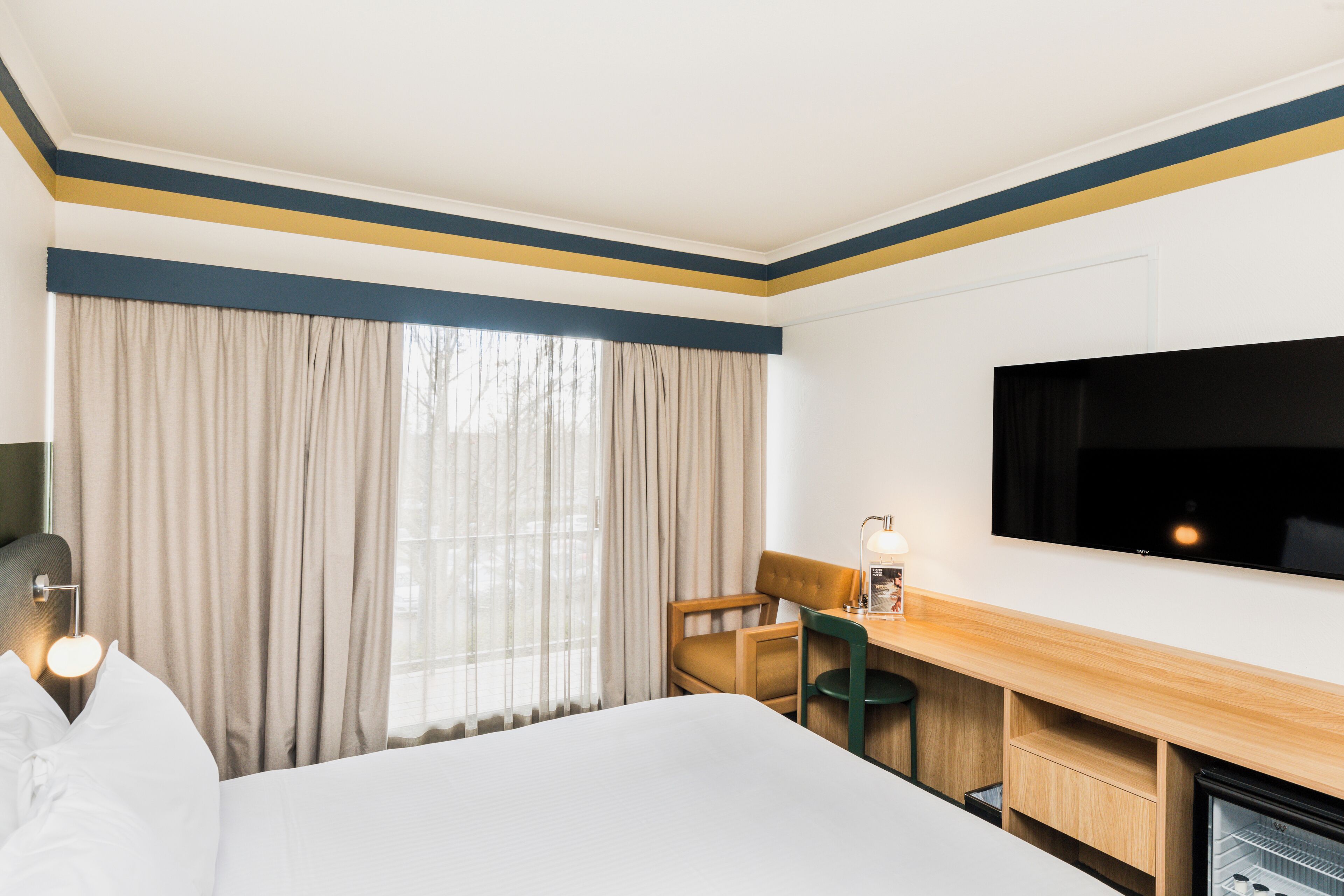 A hotel room with a bed, a desk, a chair, a television, and a minibar.