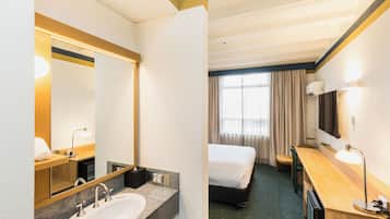 Una habitación de hotel con una cama, un escritorio, un lavamanos y un espejo.