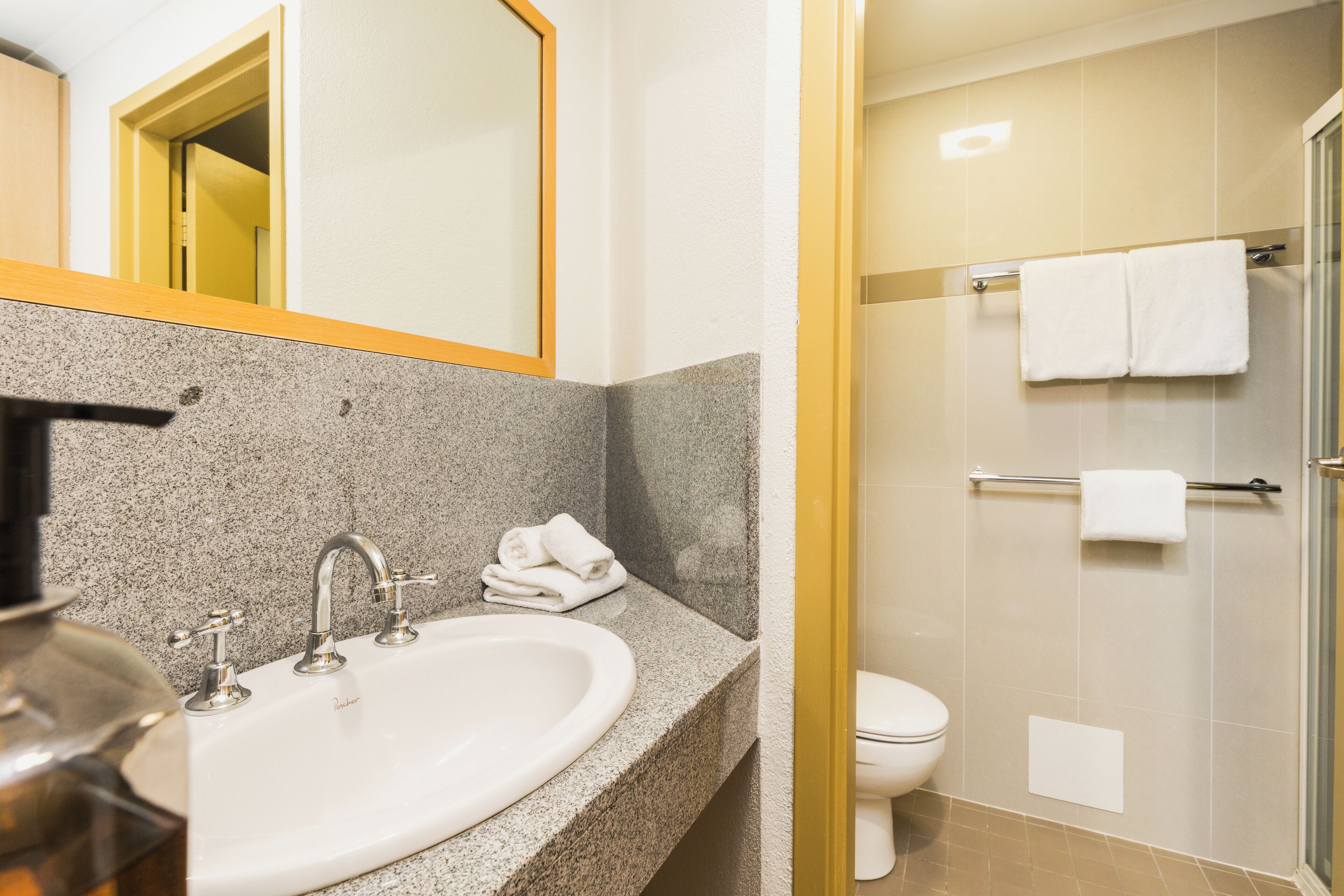 Une salle de bain avec un lavabo doté d’un plan de travail en granit, un miroir et un espace douche séparé par une porte en verre.