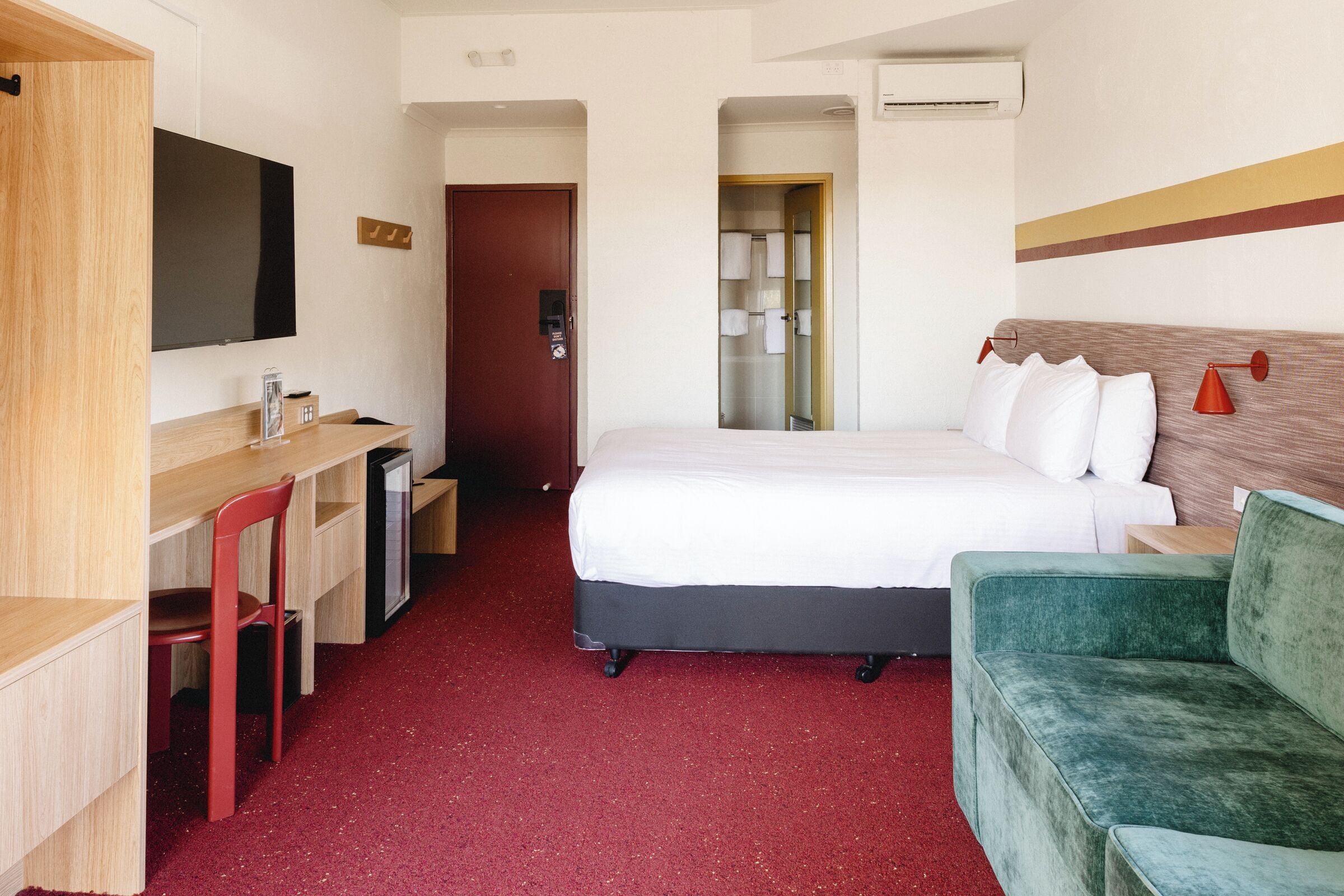 A hotel room with a bed, a desk with a chair, a TV, and a green sofa.