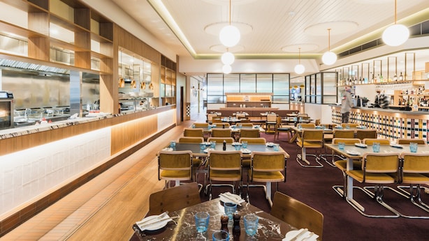 A modern restaurant with a long counter, multiple dining tables, and a bar area. - Statesman Hotel (Curtin)