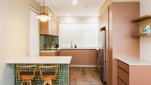 A modern kitchen with a central island, wooden chairs, a hanging light fixture, and a refrigerator. - Statesman Hotel (Curtin)