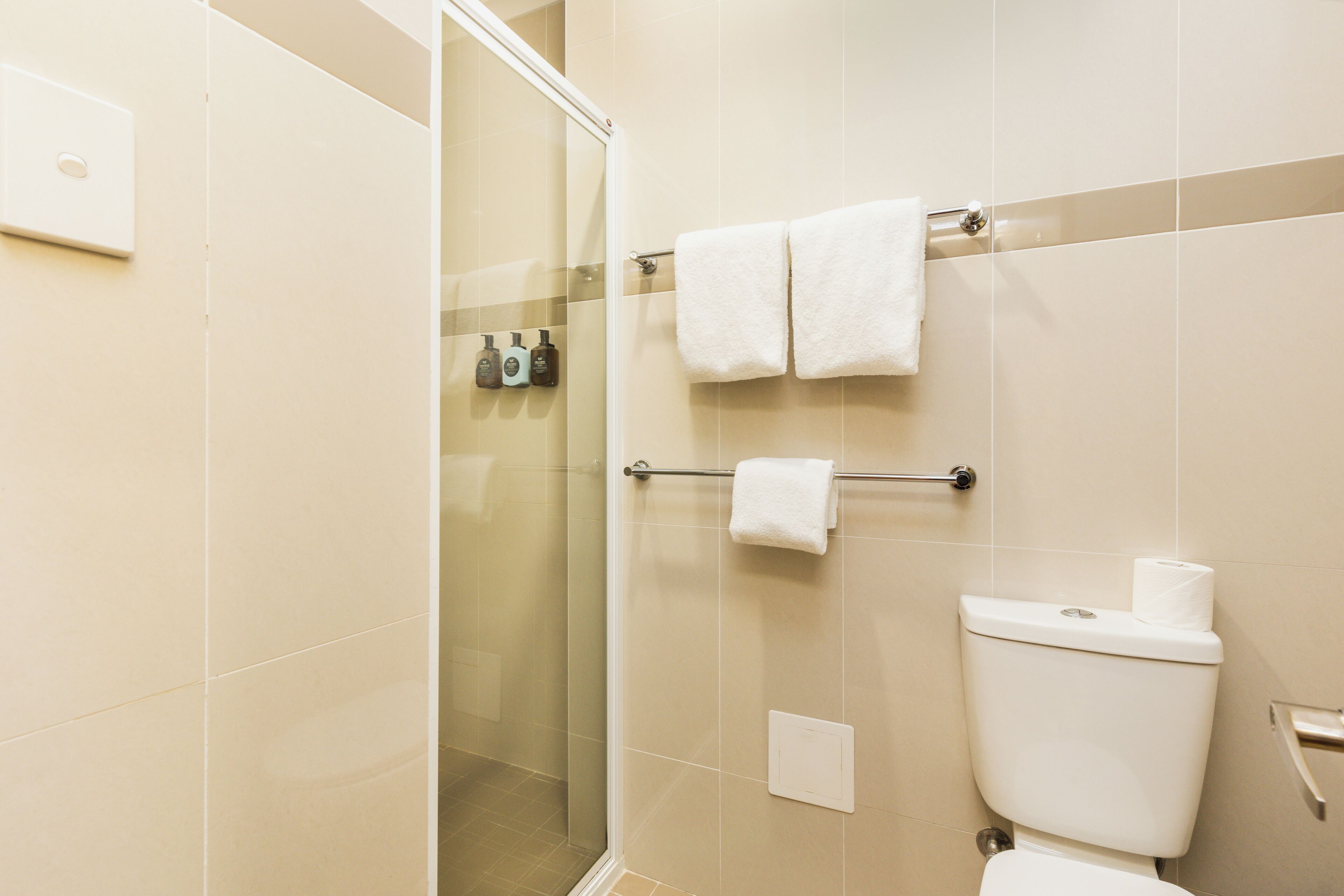 Een moderne badkamer met een glazen douchecabine, een toilet en een handdoekrek met twee handdoeken.