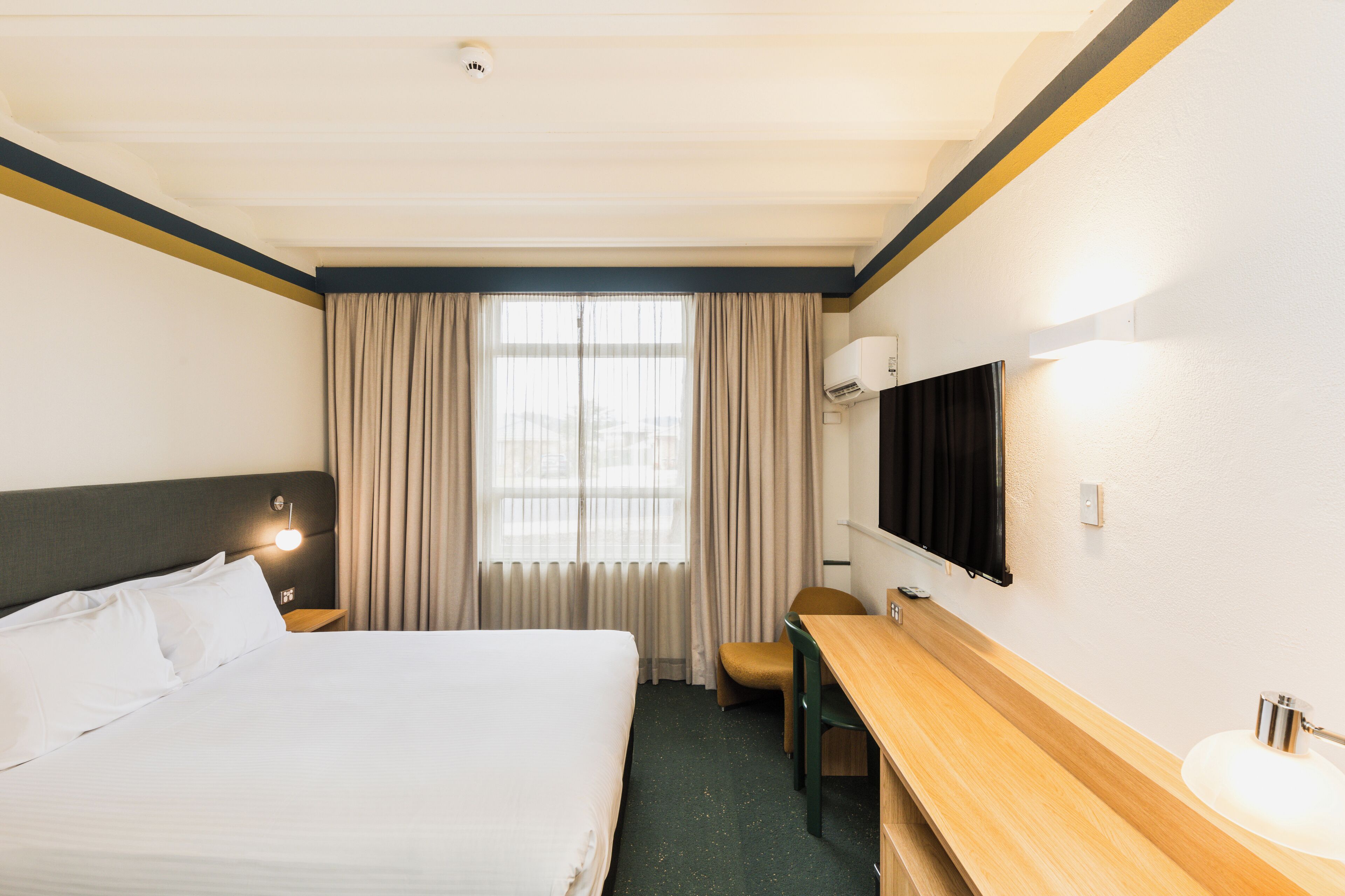 A hotel room with a bed, a desk, a chair, a TV, and a window with curtains.