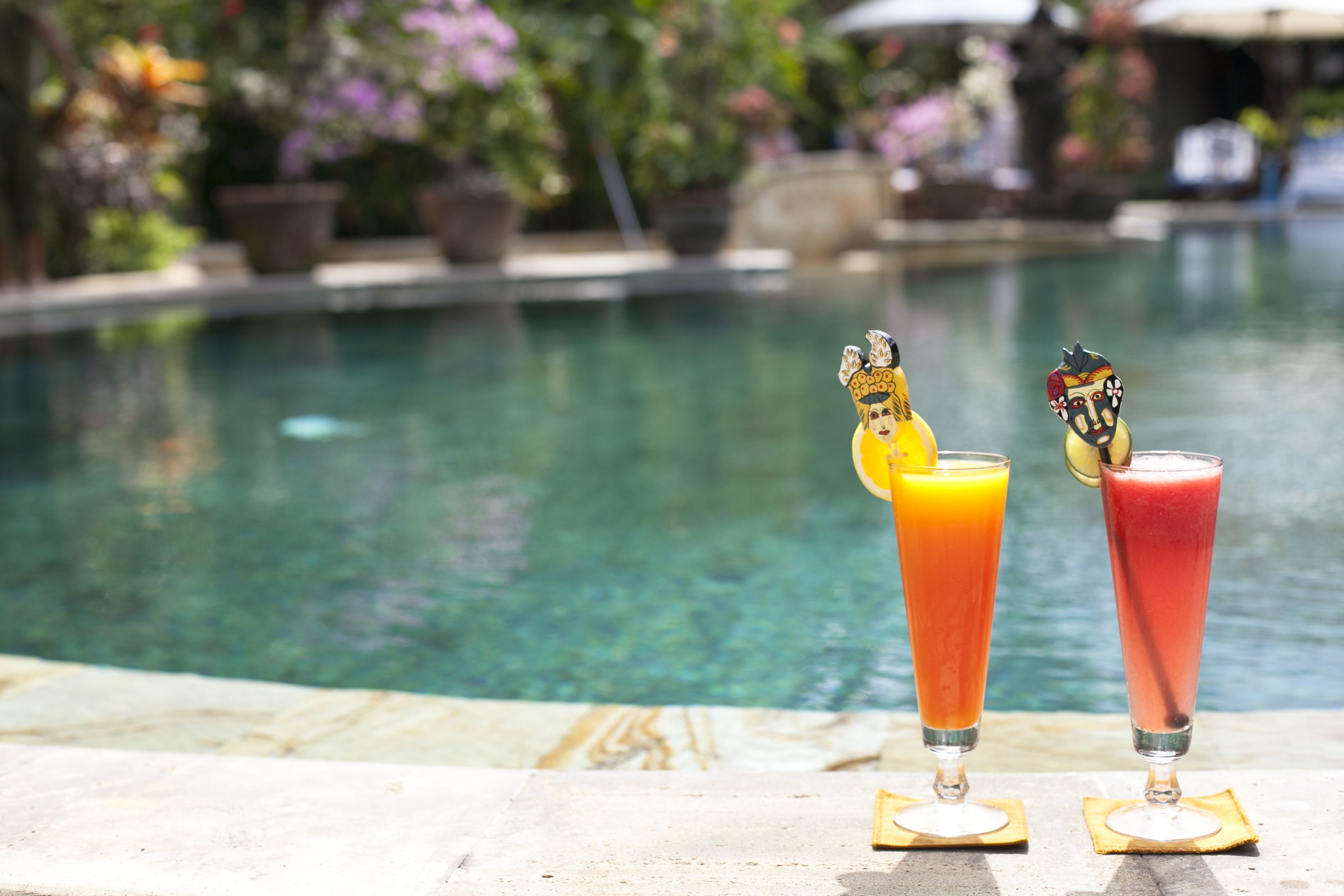 Zwei Cocktails mit dekorativen Figuren auf Untersetzern am Pool.