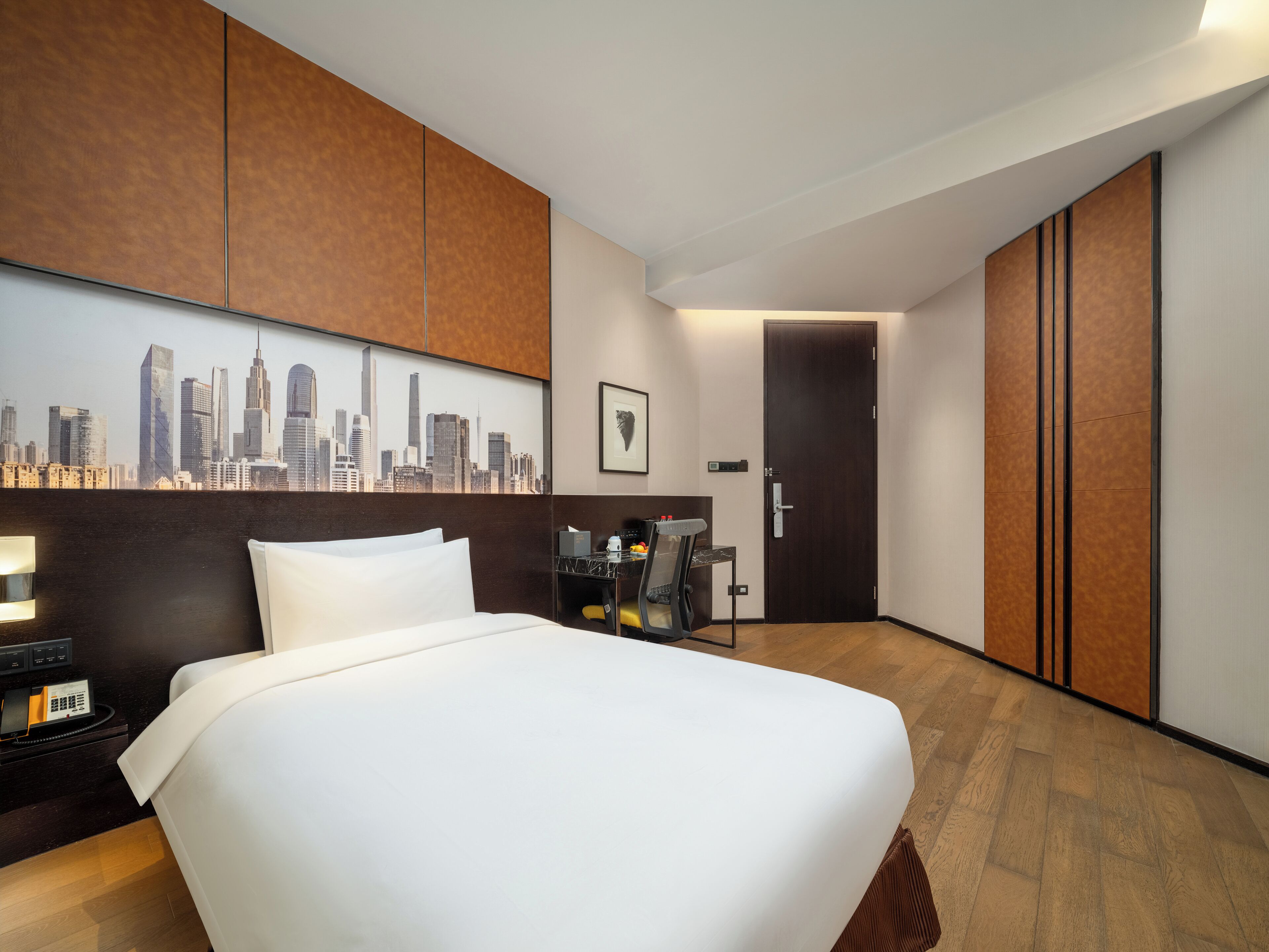 Een hotelkamer met een groot bed, een stadsgezicht muurschildering, een bureau met een stoel en een kledingkast.