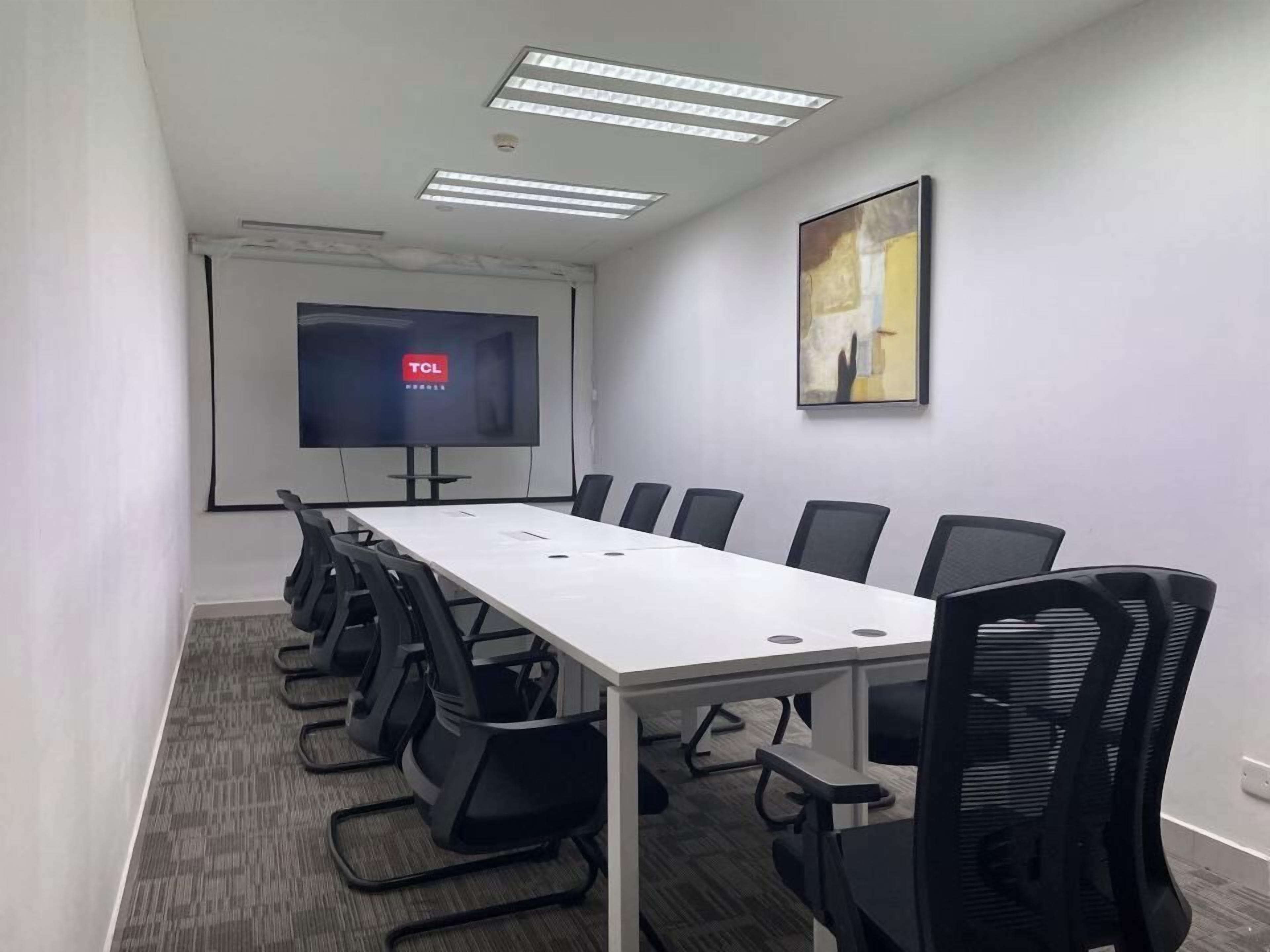 Een vergaderruimte met een lange tafel, zwarte stoelen, een projectiescherm en een schilderij aan de muur.