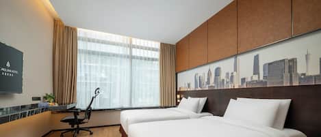 Ein Hotelzimmer mit zwei Betten, einem Schreibtisch, einem Stuhl, einem Fernseher und Blick auf die Stadt.