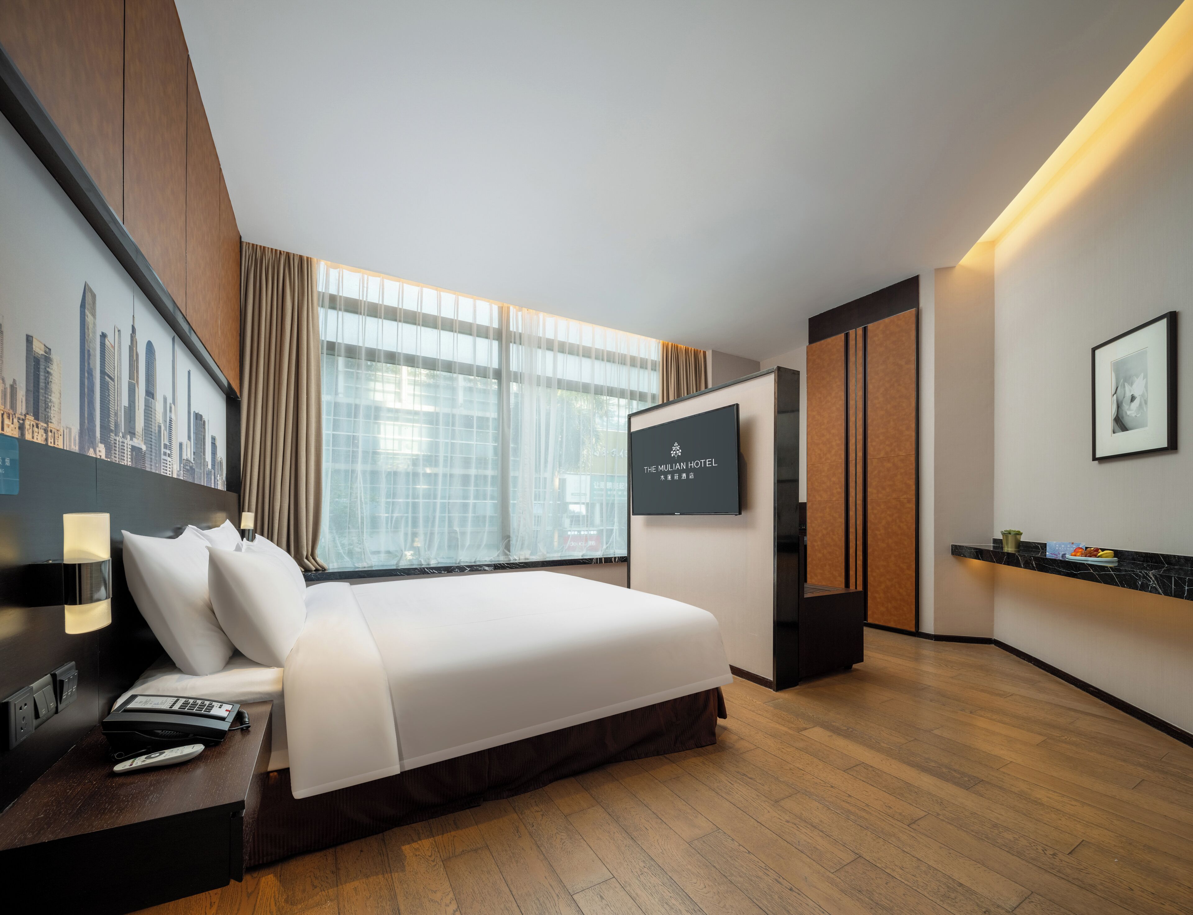 Una camera d'albergo moderna con un letto grande, una televisione a schermo piatto, una scrivania con il telefono e vista sulla città.